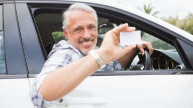 Homme souriant dans sa voiture blanche montrant sa carte grise